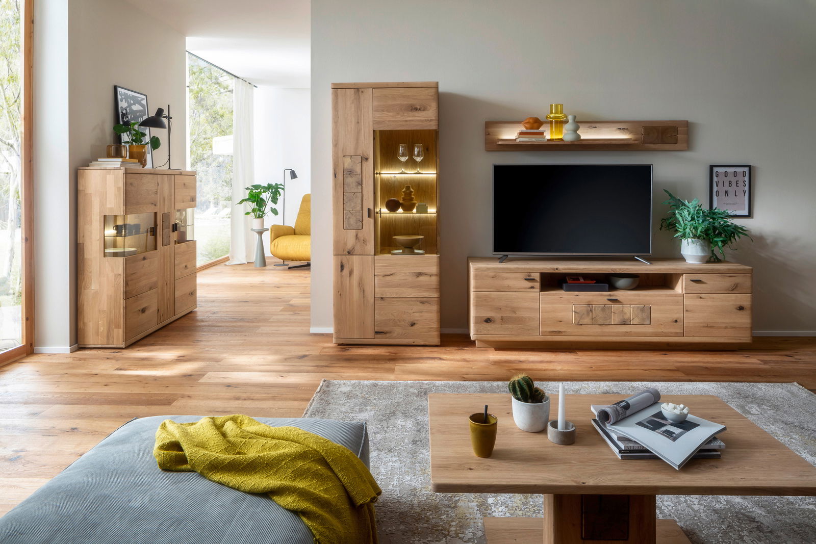 Wohnzimmer mit moderner Holzmöbelkombination, bestehend aus Vitrine, Lowboard mit Fernseher und Wandregal, aus der Perspektive von einem Couchtisch aus gesehen.