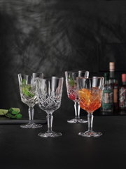 Vier elegante Cocktailgläser Noblesse mit facettiertem Design, gefüllt mit bunten Getränken, auf schwarzem Hintergrund. Frontale Perspektive.
