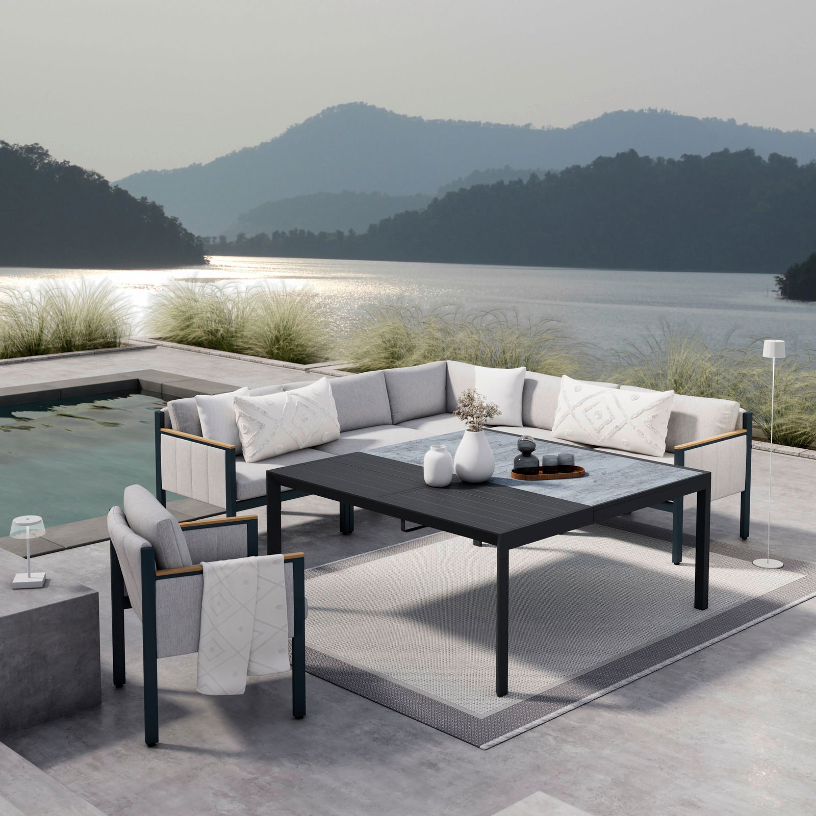 Moderne Lounge-Möbel auf einer Terrasse mit Seeblick, bestehend aus einem Ecksofa, einem Sessel und einem Gartentisch. Perspektive von schräg oben.