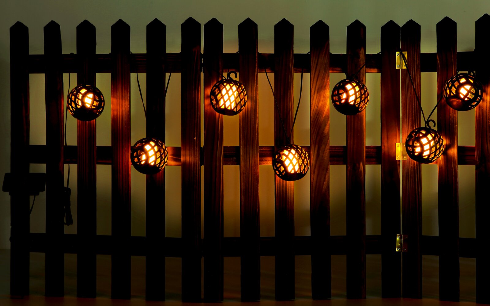 Solarbetriebene Lichterkette mit warmem Licht, aufgehängt an einem Holzzaun, seitliche Perspektive