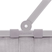 Detailaufnahme aus frontaler Perspektive: grauer Reisenthel-Tragegriff mit Gelenk und Klettverschluss an einer gerippten Stofftasche