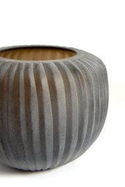 Close-up vanuit licht bovenaanzicht van een ronde, donkergrijze bloempot met verticale ribbelstructuur en warme houtkleurige binnenzijde tegen een witte achtergrond.