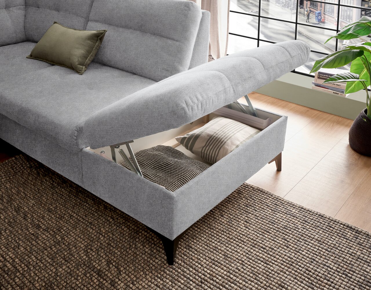 Graues Sofa mit Stauraum, geöffnet, von schräg oben fotografiert. Ein Kissen liegt auf der Sitzfläche.