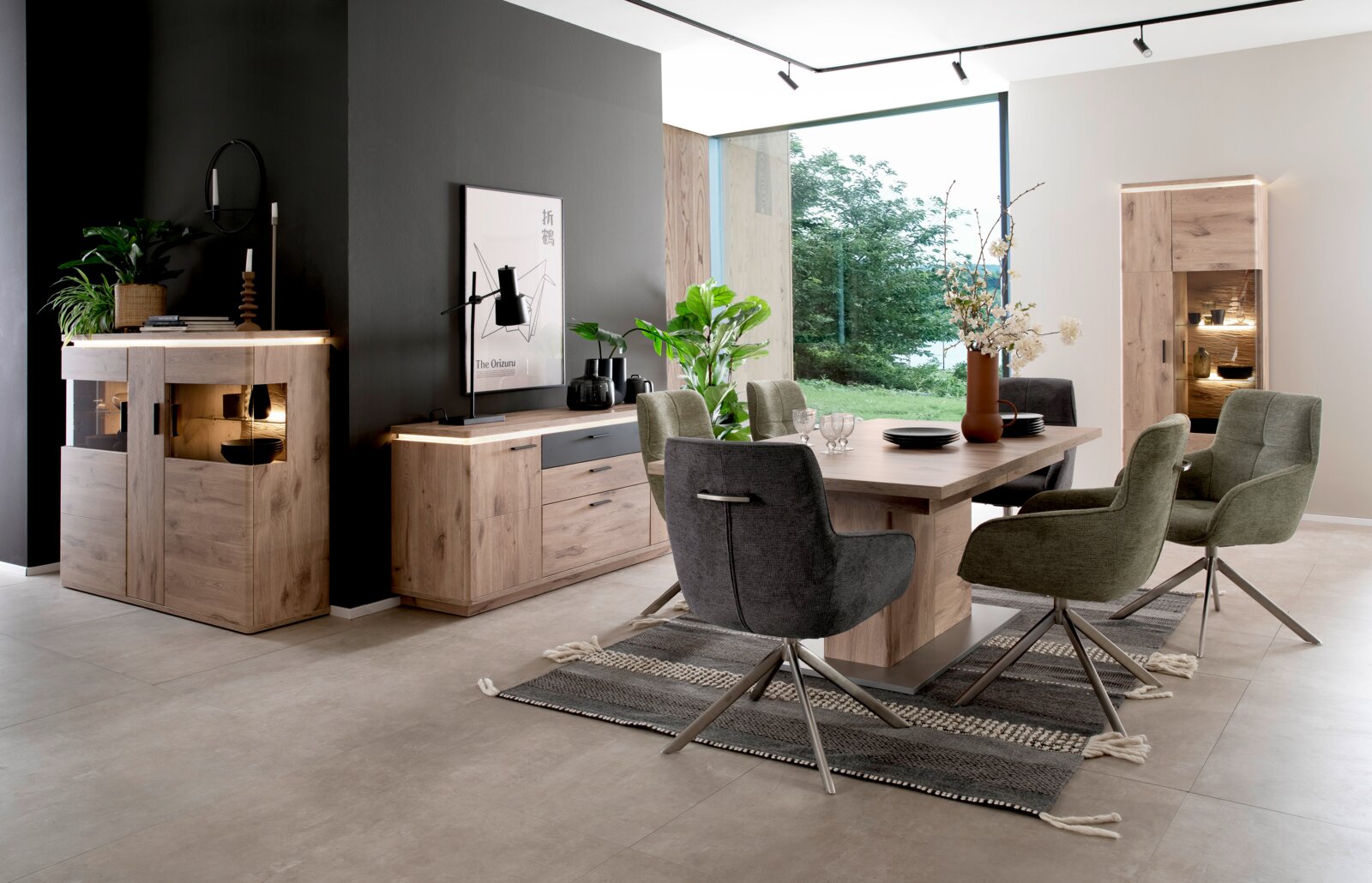 Moderne eetkamerset in eikenhoutlook met een grote eettafel, vier gestoffeerde draaistoelen, een dressoir en een verlichte vitrinekast; foto genomen vanuit een schuin vooraanzicht in een lichte woonkamer.