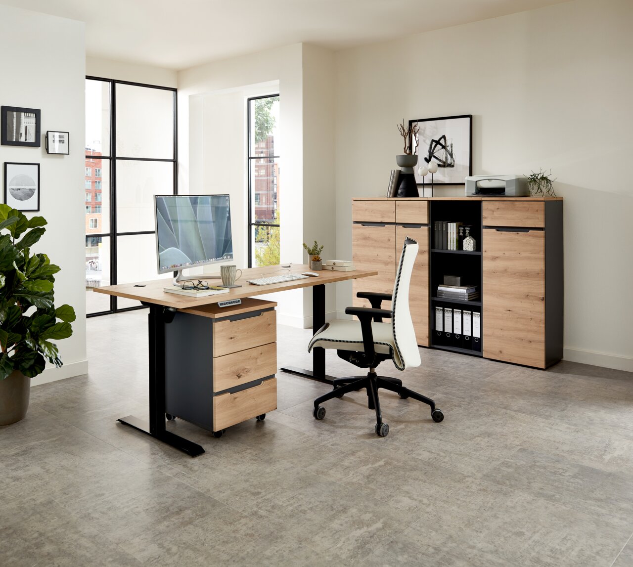 Moderner Büroraum mit Voleo E-Schreibtisch DETROIT in Holzoptik, Rollcontainer und ergonomischem Bürostuhl, seitliche Perspektive.