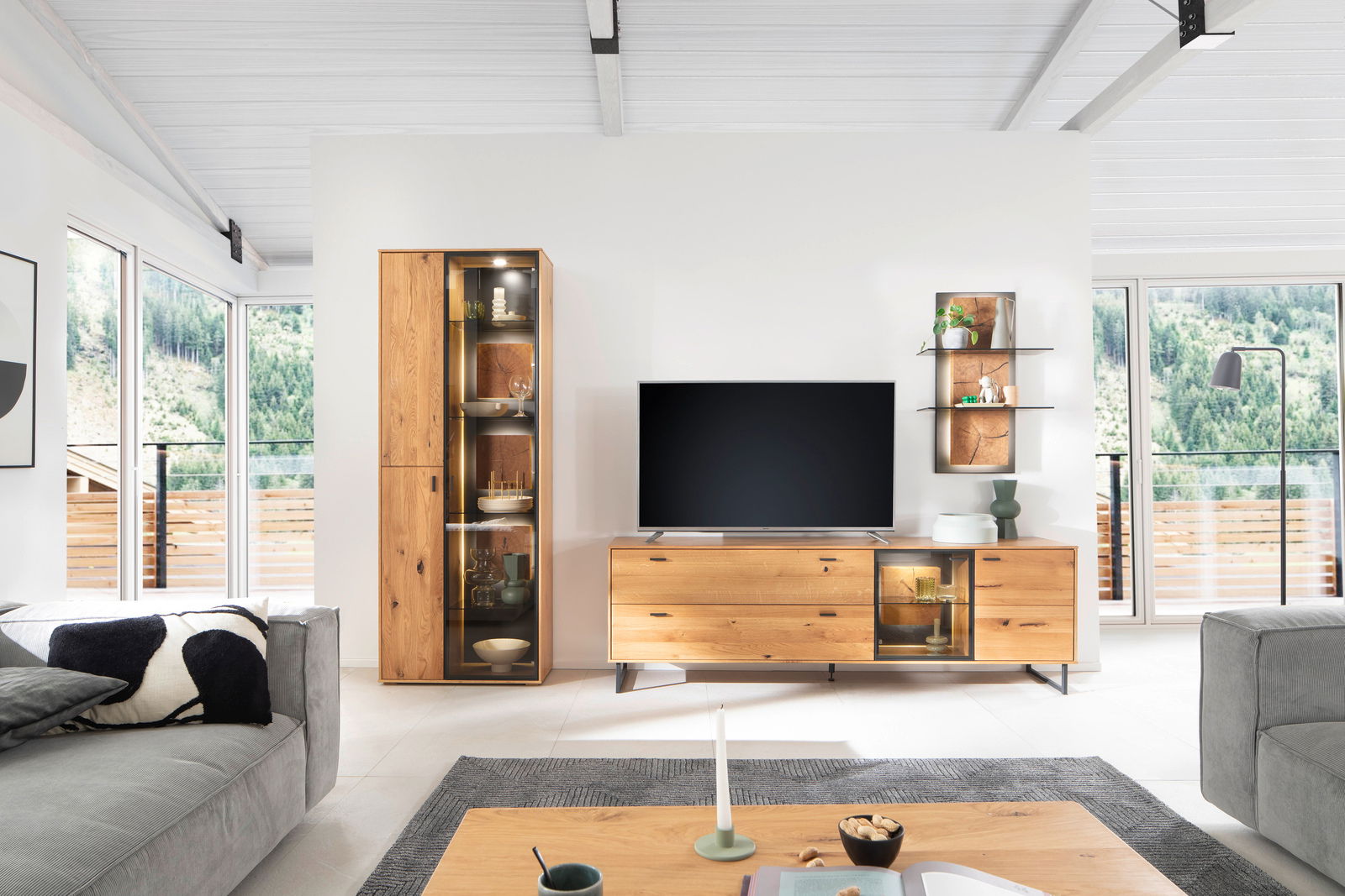Moderne Wandkombination aus Holz mit Vitrine, TV-Schrank und Wandregal in einem hellen Wohnzimmer mit Blick auf die Berge.