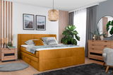 Gemütliches Schlafzimmer mit einem senfgelben Boxspringbett, umgeben von modernen Holzmöbeln und Pflanzen, aus der Perspektive von vorne rechts.