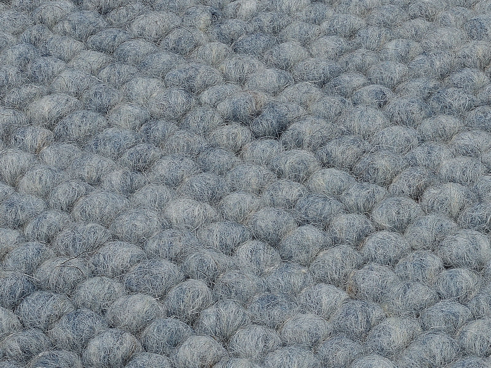 Nahaufnahme eines handgewebten Teppichs mit einer texturierten, grauen Oberfläche in Kugeloptik.