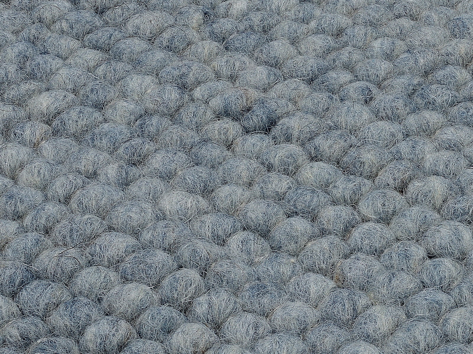 Nahaufnahme eines handgewebten Teppichs mit einer texturierten, grauen Oberfläche in Kugeloptik.