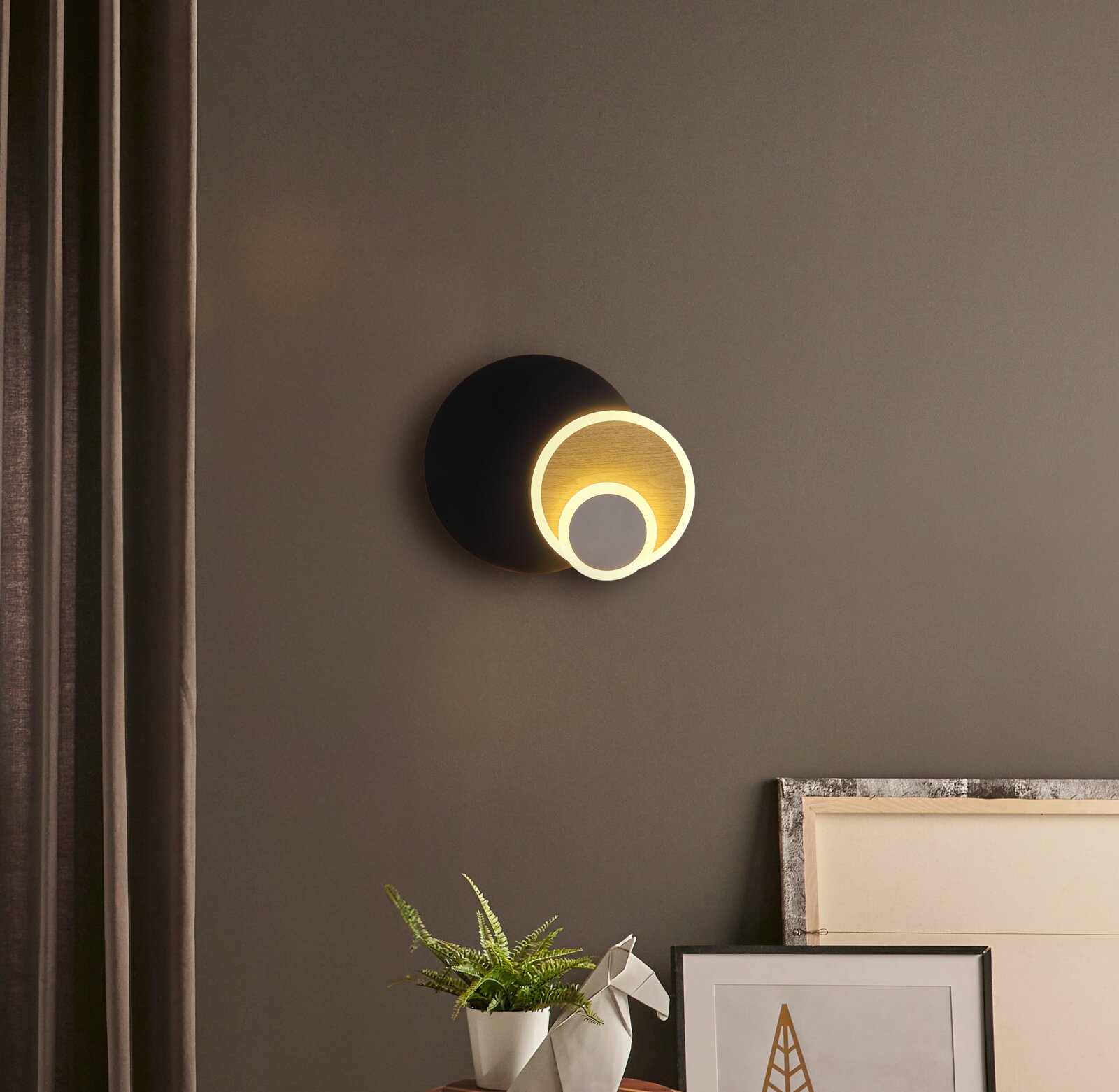 Moderne LED-Wandleuchte mit zwei leuchtenden Ringen, schwarzer runder Wandhalterung und warmweißem Licht an grauer Wand, frontale Ansicht.