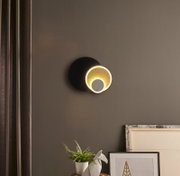 Moderne LED-Wandleuchte mit zwei leuchtenden Ringen, schwarzer runder Wandhalterung und warmweißem Licht an grauer Wand, frontale Ansicht.