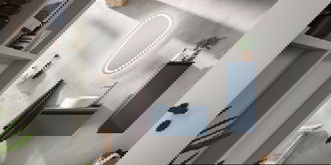 Kleines Bad mit blauem Schrank, rundem Spiegel und Waschbecken auf Betonwand.