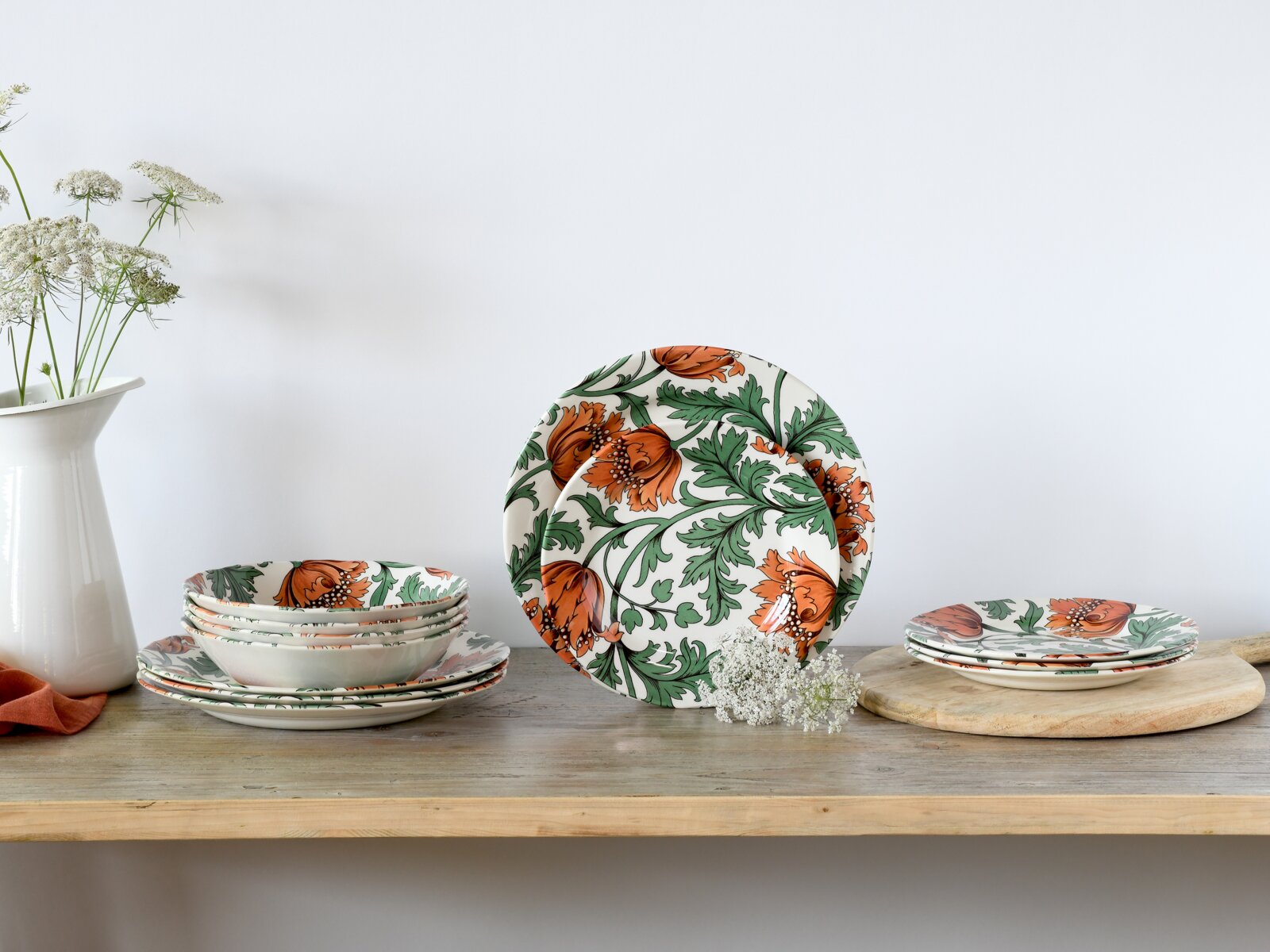 Florales Geschirrset aus Keramik mit orangefarbenen Blüten und grünen Ranken, Teller und Schalen auf Holztisch arrangiert, perspektivisch in leichter Frontalansicht mit zentral aufgestelltem Teller
