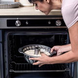 Eine Person schiebt eine gefüllte Gugelhupfform in einen Backofen. Die Perspektive zeigt die Szene von der Seite.