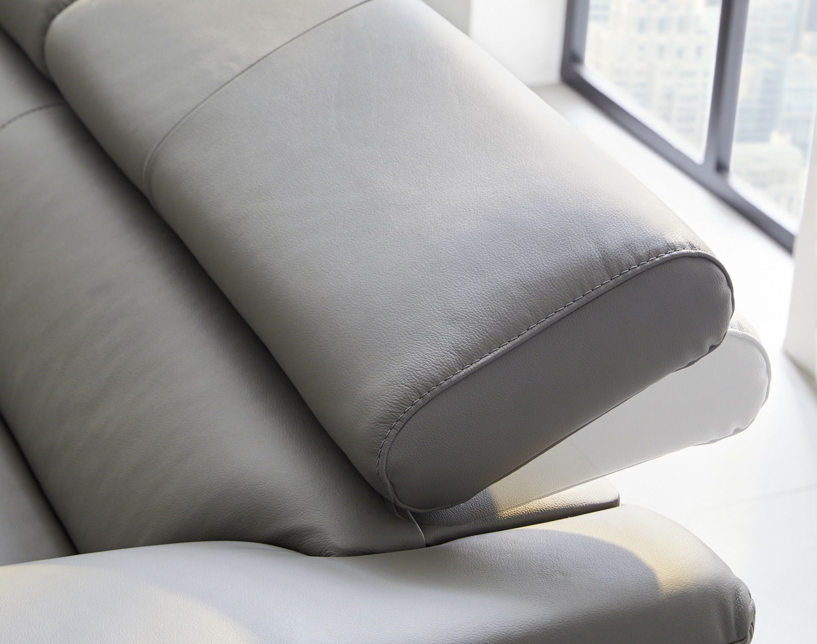Nahaufnahme einer grauen Ledercouch mit verstellbarer Kopfstütze, seitliche Perspektive.