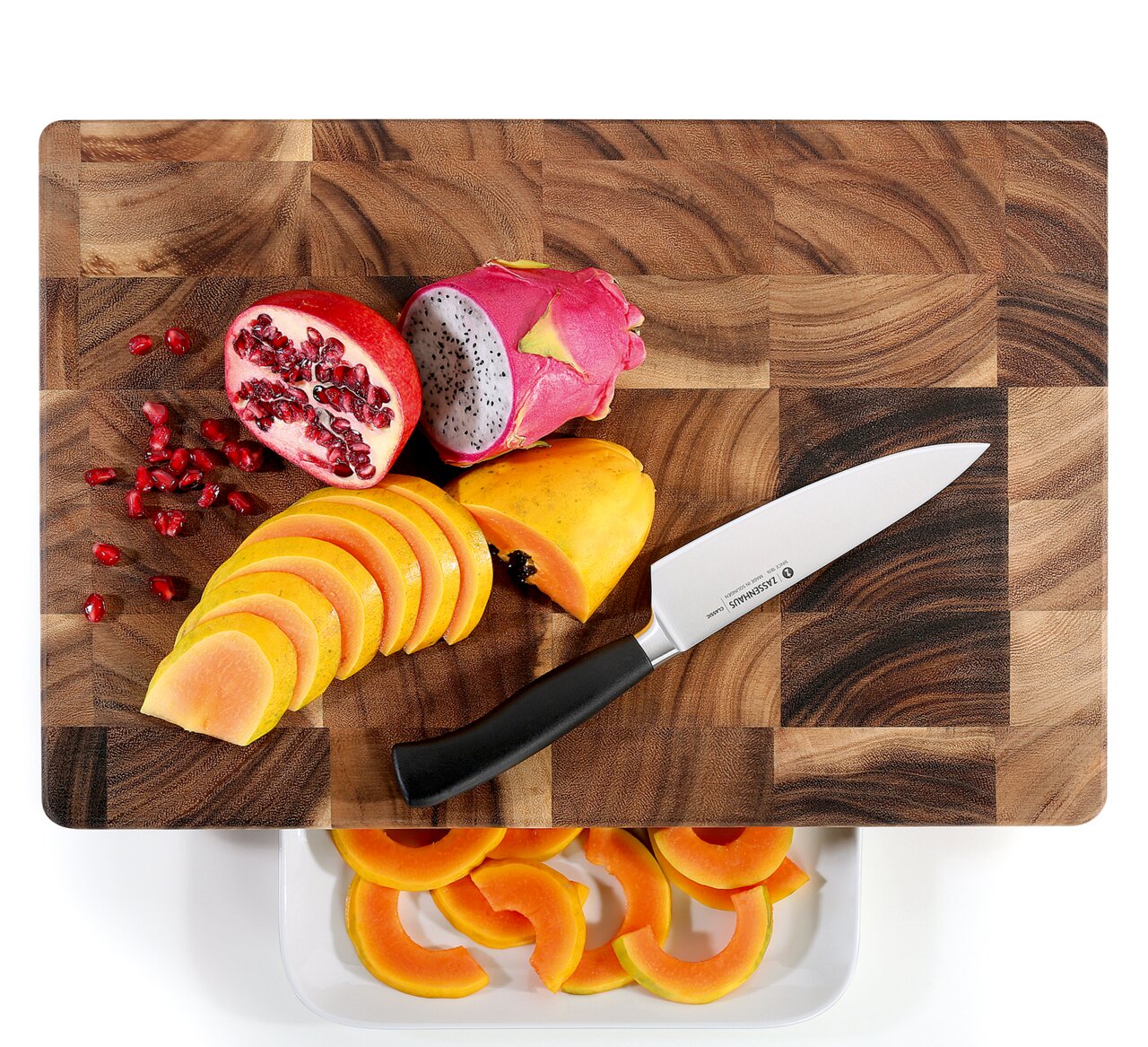 Vogelperspektive auf einen Hackblock aus Akazienholz mit geschnittenem Obst und einem Messer.