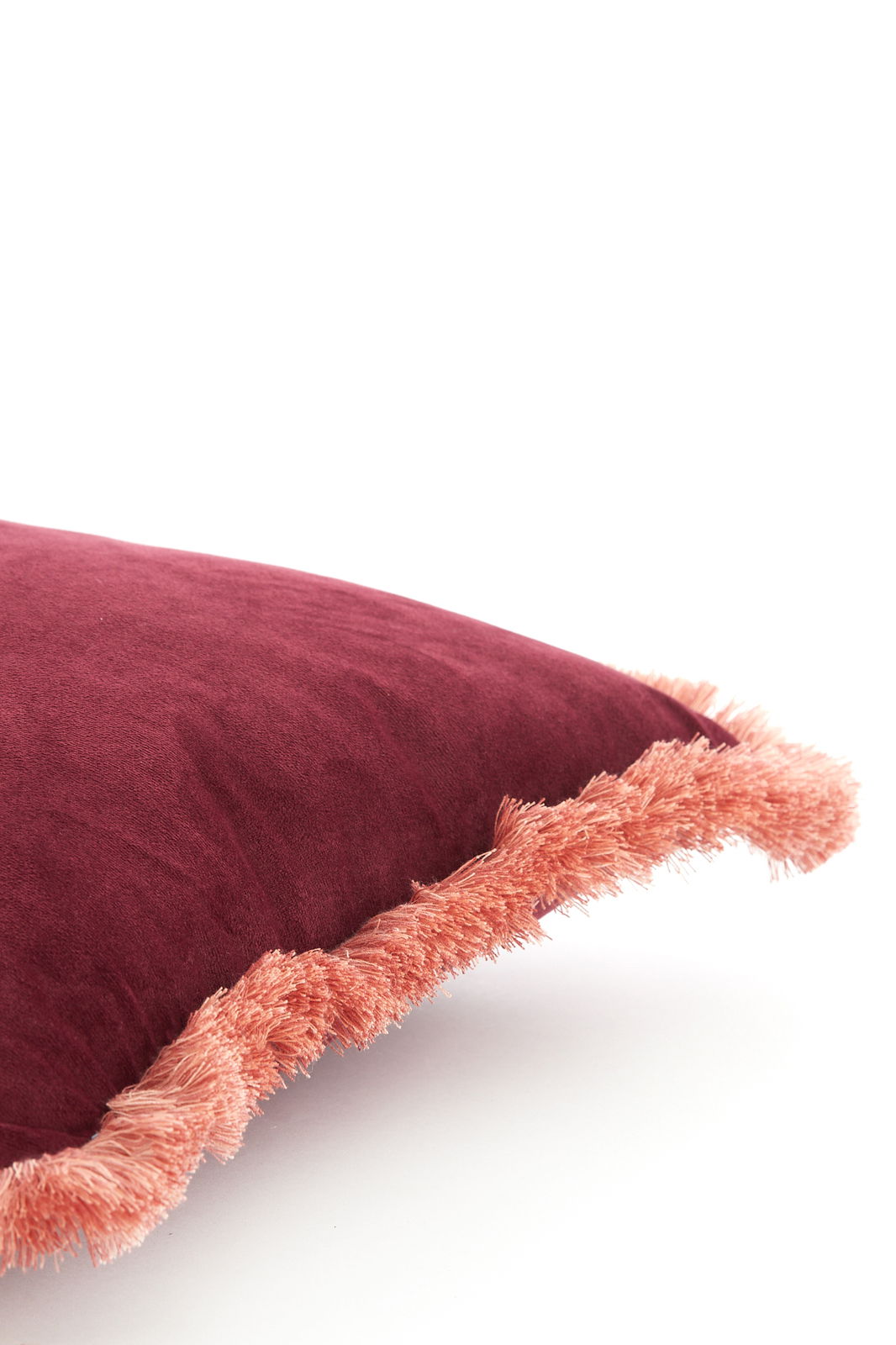 Nahaufnahme eines weinroten Kissens mit rosa Fransen, seitliche Perspektive