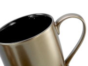 Nahaufnahme einer metallisch goldfarbenen Tasse mit schwarzer Innenseite und großem Henkel, leicht schräg von oben fotografiert vor weißem Hintergrund