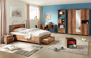 Schlafzimmer mit Holzmöbeln, bestehend aus einem Bett mit Unterbettschubkasten, einem Schreibtisch, einem Drehtürenschrank und einer Nachtkommode. Perspektive von vorne links.