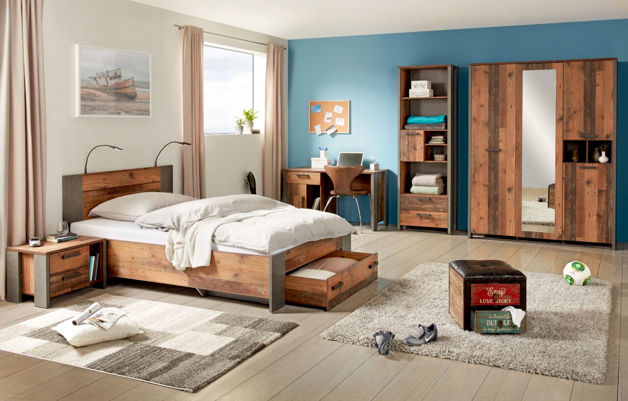 Schlafzimmer mit Holzmöbeln, bestehend aus einem Bett mit Unterbettschubkasten, einem Schreibtisch, einem Drehtürenschrank und einer Nachtkommode. Perspektive von vorne links.