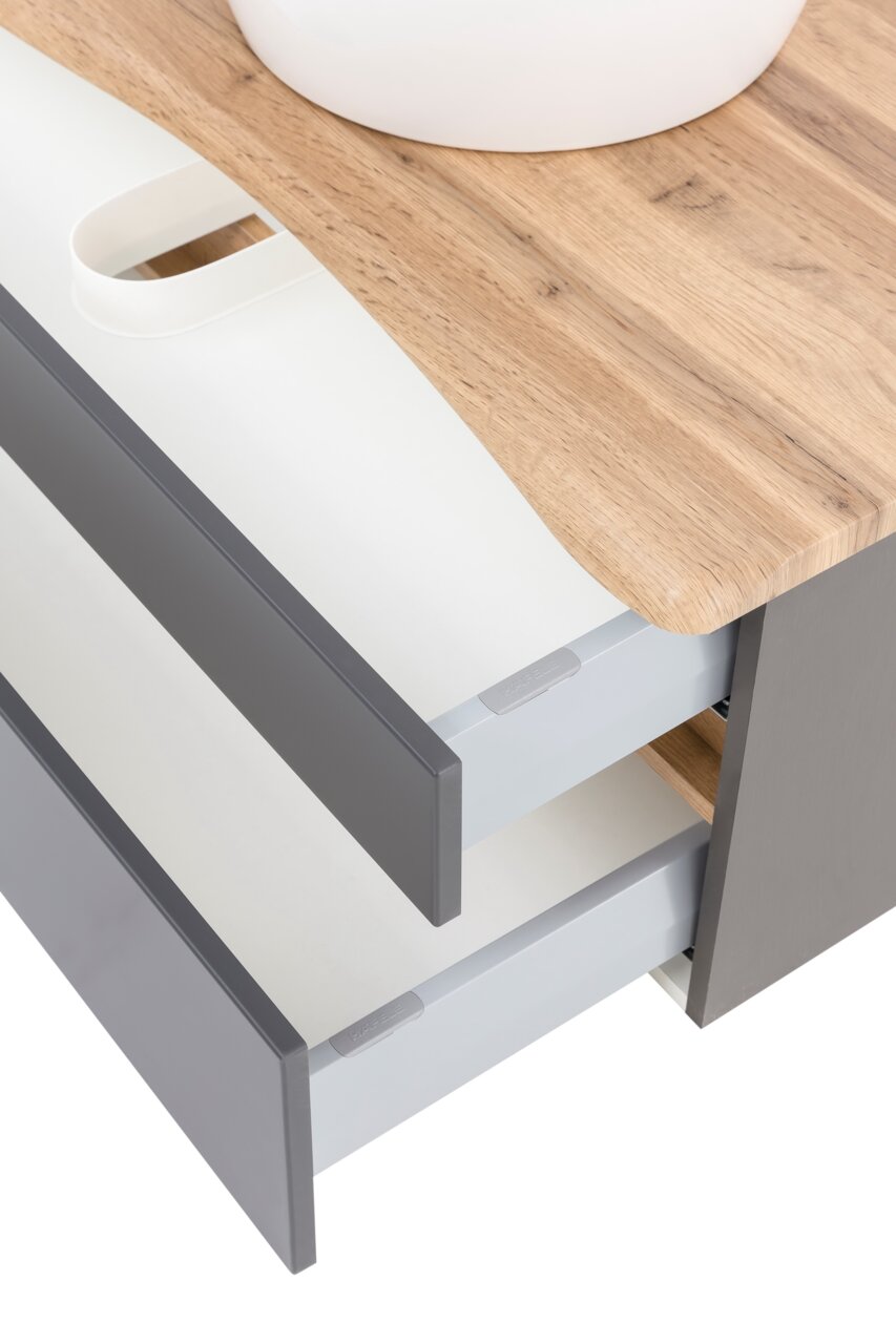 Close-up van een wastafelmeubel met houten blad en grijze lades, gezien van bovenaf.