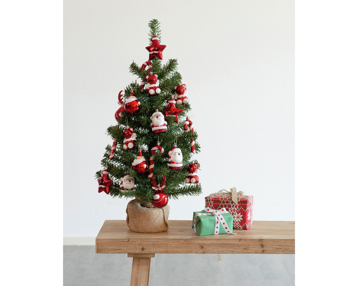 Kleiner geschmückter Weihnachtsbaum mit roten und weißen Dekorationen, auf einem Holztisch stehend, mit Geschenken daneben, aus frontaler Perspektive.