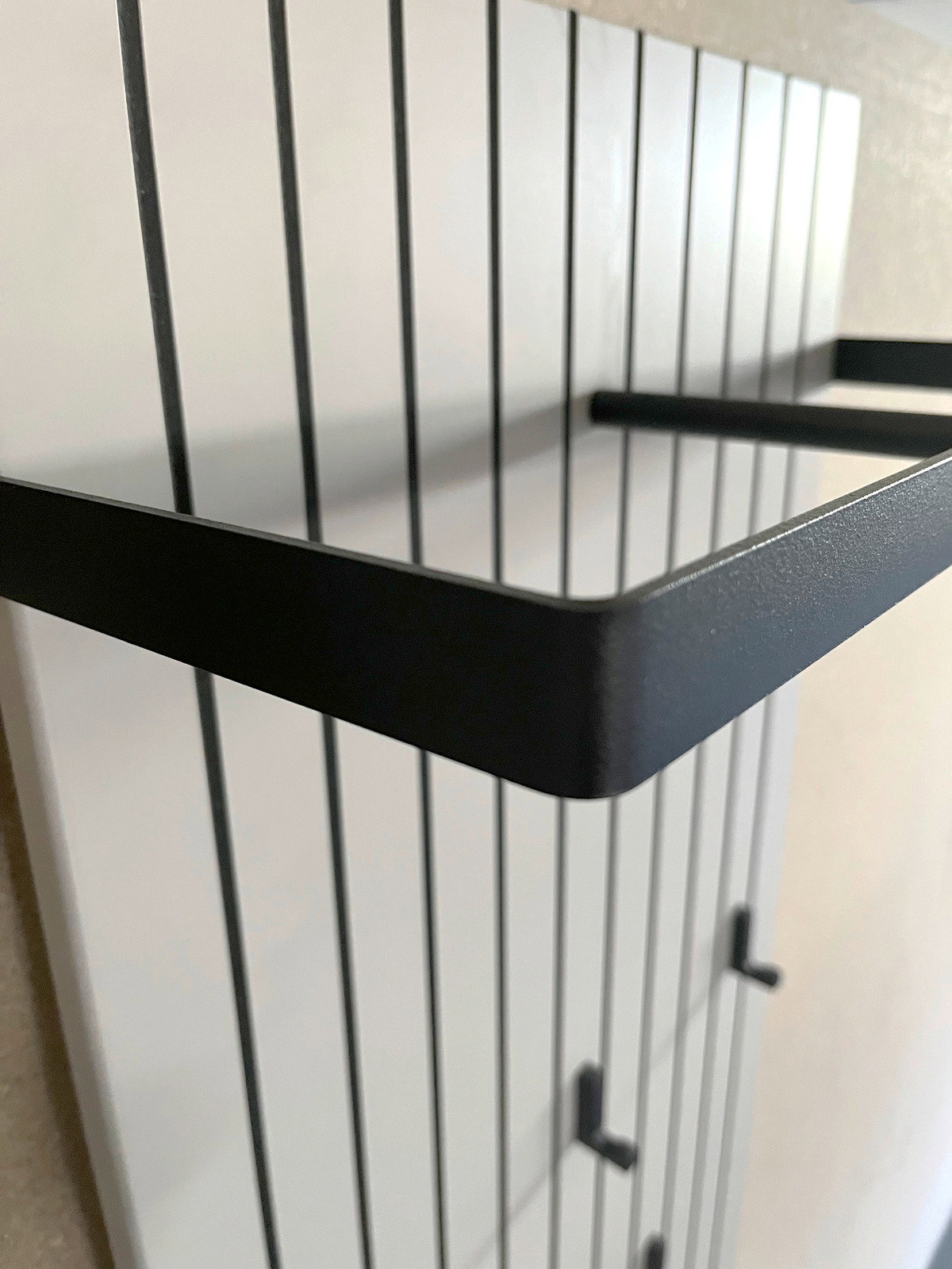 Nahaufnahme eines modernen Garderobenpaneels mit schwarzen Metallhaken und Ablage, seitliche Perspektive.