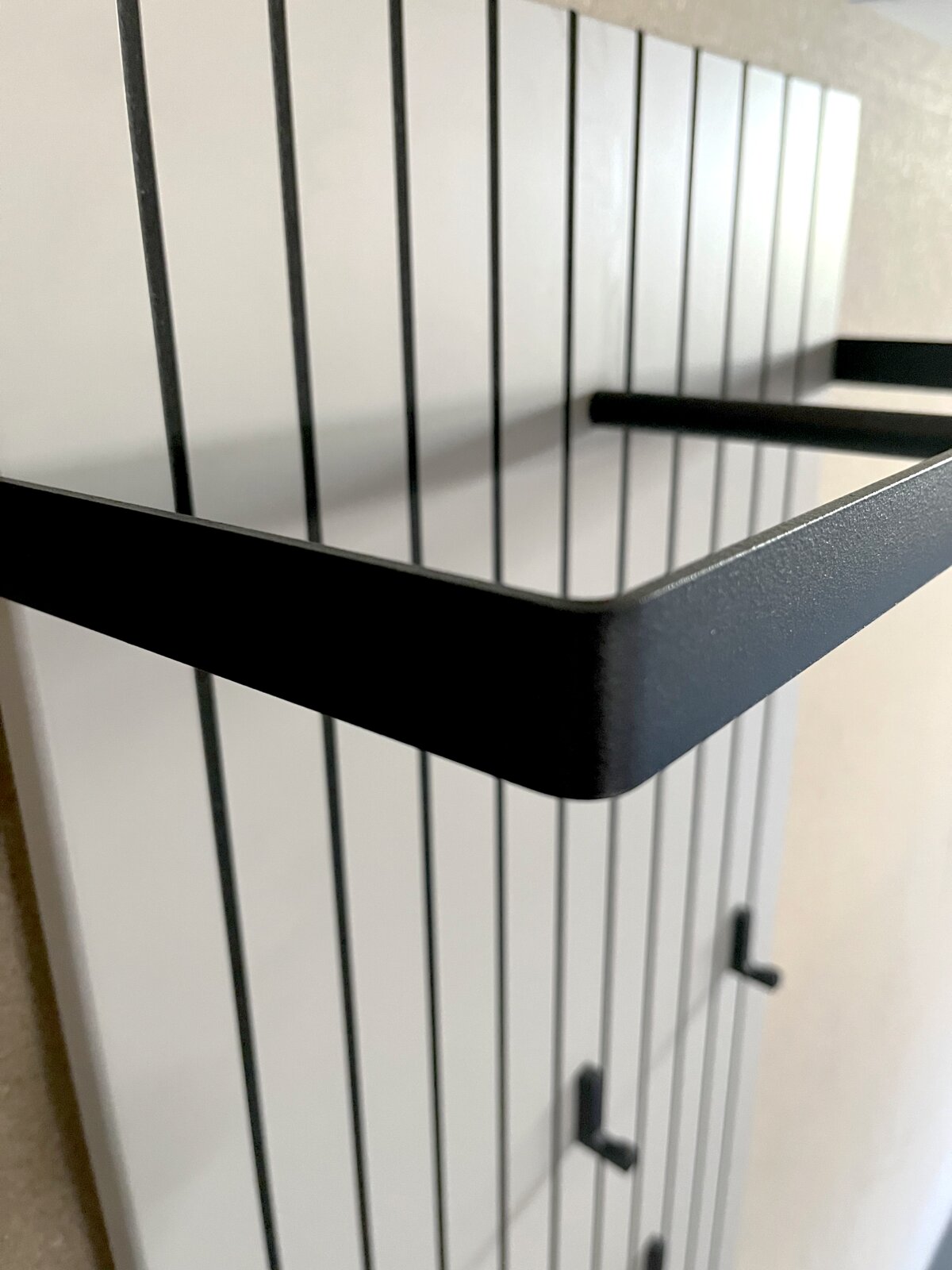 Nahaufnahme eines modernen Garderobenpaneels mit schwarzen Metallhaken und Ablage, seitliche Perspektive.