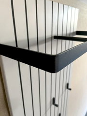 Nahaufnahme eines modernen Garderobenpaneels mit schwarzen Metallhaken und Ablage, seitliche Perspektive.