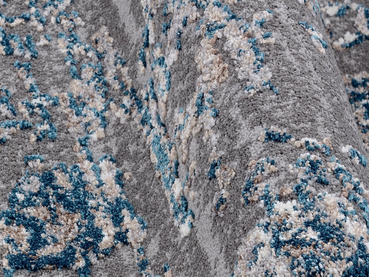 Nahaufnahme eines Designer-Teppichs mit grauem Hintergrund und blauen sowie beigen Akzenten, aus seitlicher Perspektive aufgenommen.