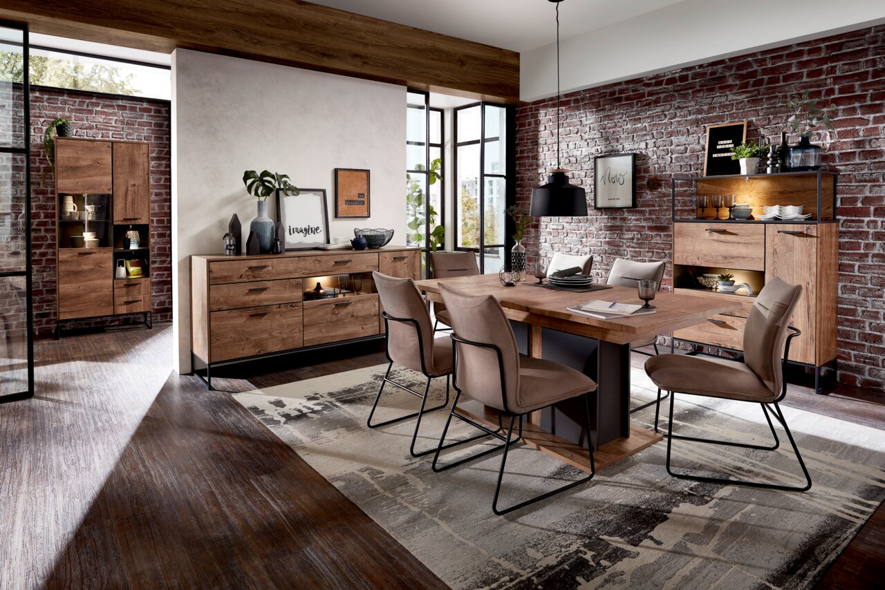 Moderne Esszimmerkombination mit Holztisch, Stühlen und Sideboards in einem stilvollen Raum mit Backsteinwänden, aus der Perspektive des Raumes betrachtet.