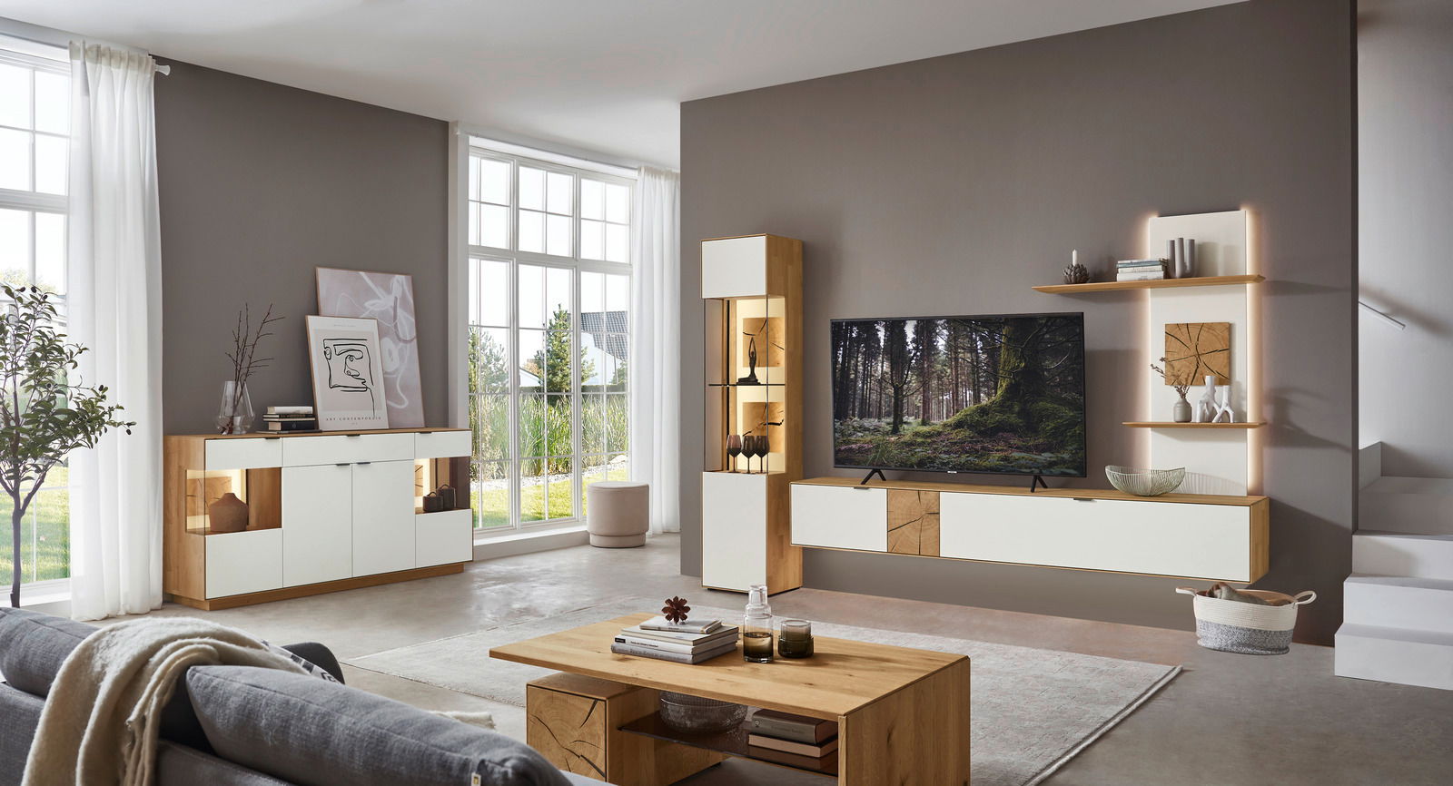 Moderne Wohnzimmermöbelkombination in heller, geräumiger Umgebung mit Sideboard, Highboard und TV-Wand in Holz- und Weißtönen, seitliche Perspektive.