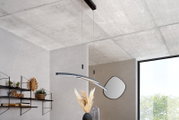 Moderne, gebogene LED-Pendelleuchte in Schwarz und Silber mit warmweißem Licht, an dünnen Seilen von der Decke abgehängt, in einem minimalistischen Wohnraum; Perspektive: leicht von unten im Raum nach oben zur Decke fotografiert.