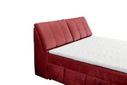 Seitliche Ansicht eines roten Boxspringbetts mit gepolstertem Kopfteil und weißer Matratze.