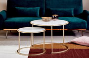 Zweier-Set von Beistelltischen mit goldenen Rahmen und weißen Tischplatten, vor einem grünen Sofa, aus der Frontalperspektive fotografiert.