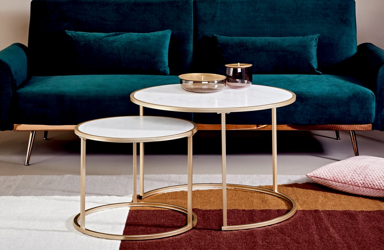 Jahnke Salontafelset SOL Set van twee bijzettafels met gouden frames en witte tafelbladen, voor een groene bank, gefotografeerd vanuit een vooraanzicht.
