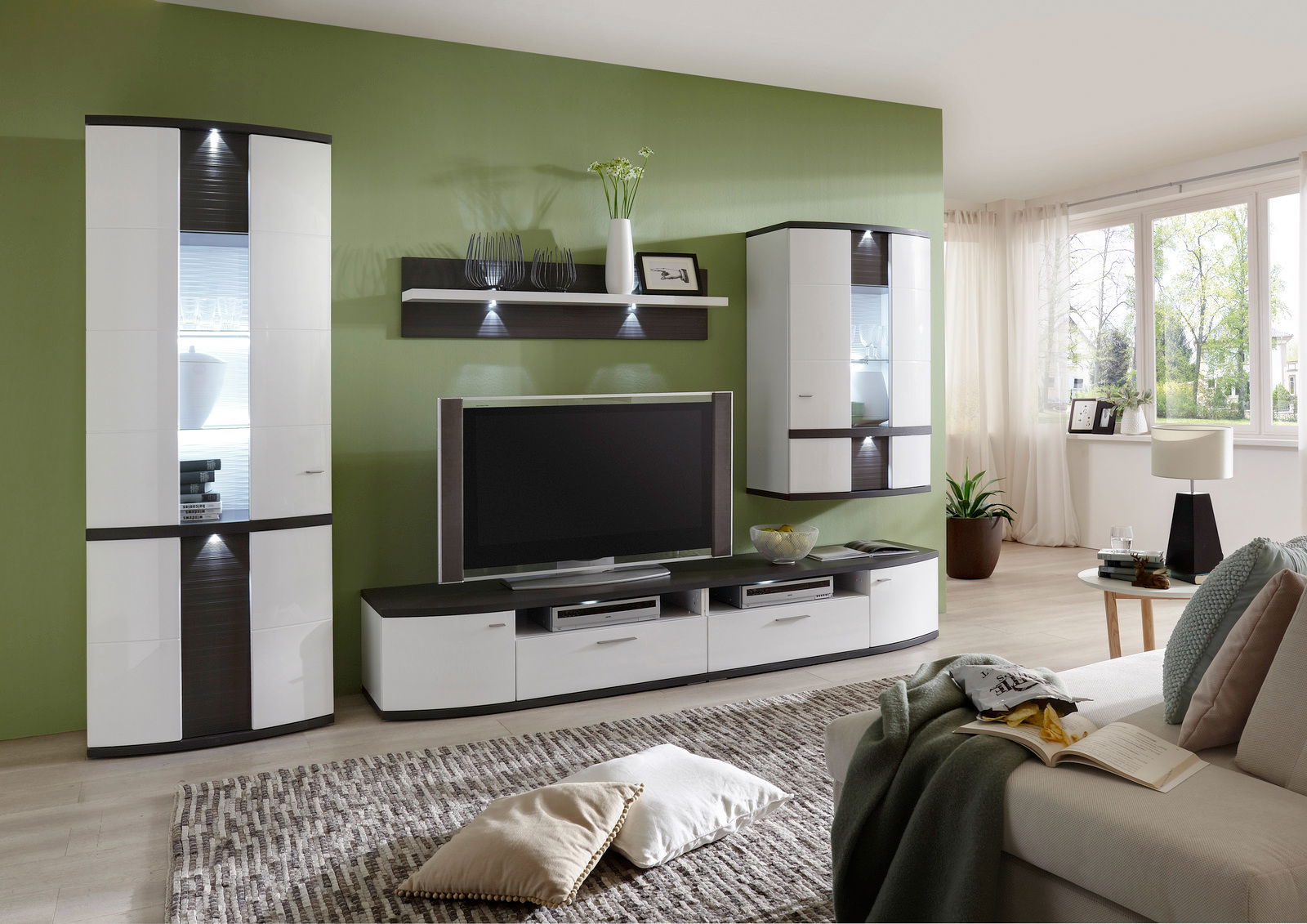 Zurbrüggen Wandpaneel CABANA Modernes Wohnzimmer mit grün gestrichener Wand, ausgestattet mit einem eleganten Wandpaneel, das über einem Fernseher montiert ist. Perspektive von der Seite, die den gesamten Raum zeigt.