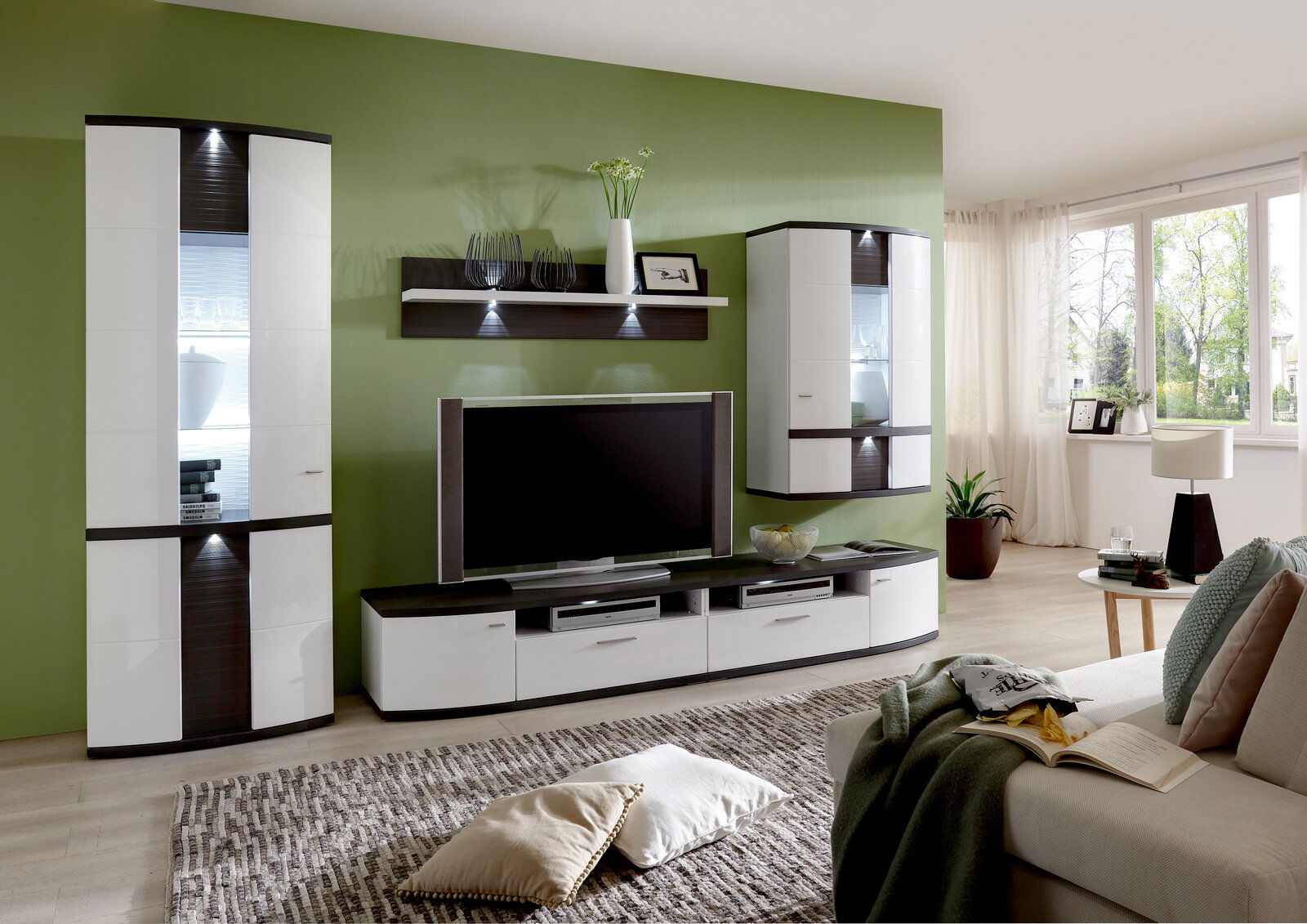 Zurbrüggen Wandpaneel CABANA Modernes Wohnzimmer mit grün gestrichener Wand, ausgestattet mit einem eleganten Wandpaneel, das über einem Fernseher montiert ist. Perspektive von der Seite, die den gesamten Raum zeigt.