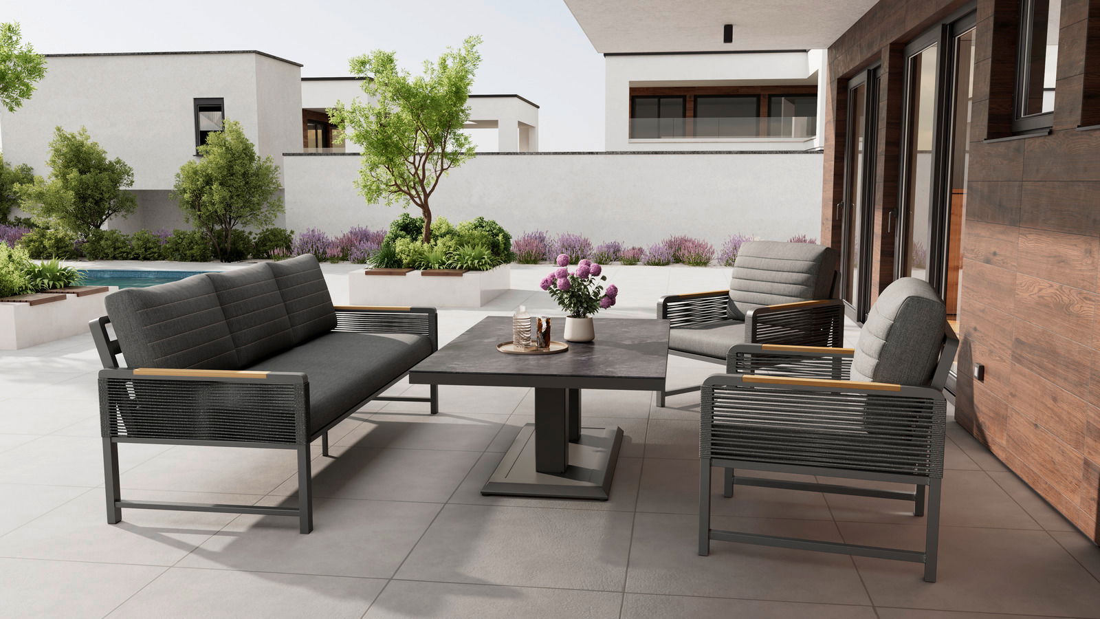 Ambia Garden Tweezitsbank CALIDA Moderne Loungegarnitur auf einer Terrasse mit Blick auf einen Garten, bestehend aus einem Tisch, einem Sofa und Sesseln in stilvollem Design.