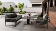 Moderne Loungegarnitur auf einer Terrasse mit Blick auf einen Garten, bestehend aus einem Tisch, einem Sofa und Sesseln in stilvollem Design.
