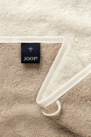 Nahaufnahme eines beigen Handtuchs mit einem schwarzen Joop!-Etikett, das auf der Innenseite sichtbar ist.