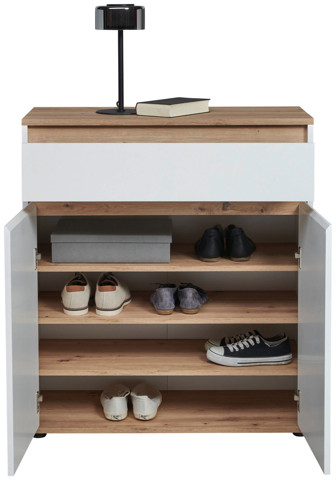 Kommode mit weißer Front und Holzoberfläche, offene Türen zeigen mehrere Regalböden mit Schuhen und einer Box, darauf eine Lampe und ein Buch, frontale Perspektive
