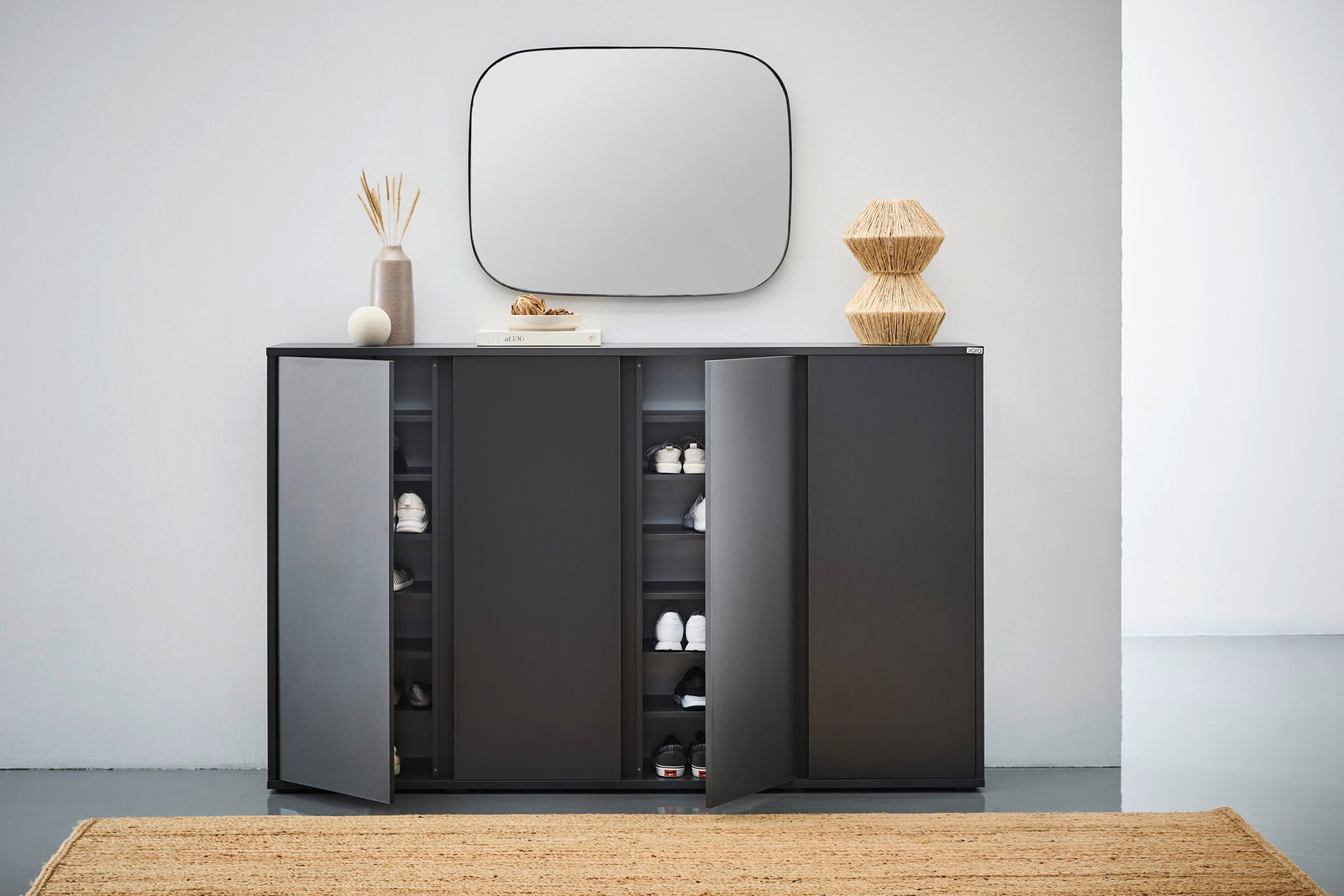 Moderner schwarzer Schuhschrank mit geöffneten Türen, gefüllt mit Schuhen, aus frontaler Perspektive fotografiert. Dekorative Elemente wie ein Spiegel und Vasen auf der Oberseite.