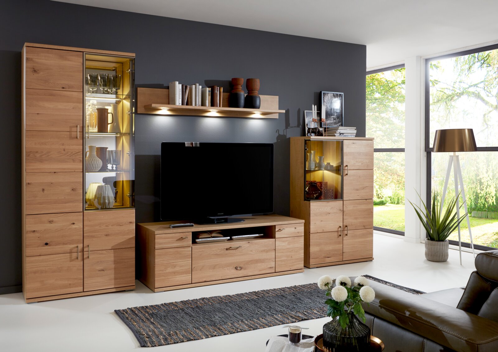 Moderne Wandkombination aus Holz mit Vitrinen und TV-Schrank in einem hellen Wohnzimmer, seitliche Perspektive.