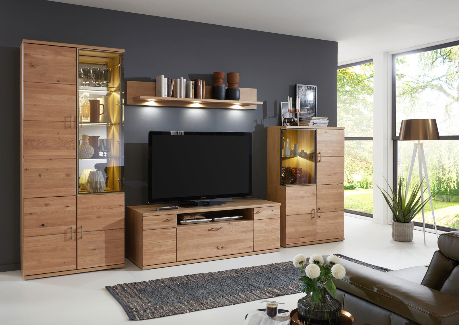 Moderne Wandkombination aus Holz mit Vitrinen und TV-Schrank in einem hellen Wohnzimmer, seitliche Perspektive.