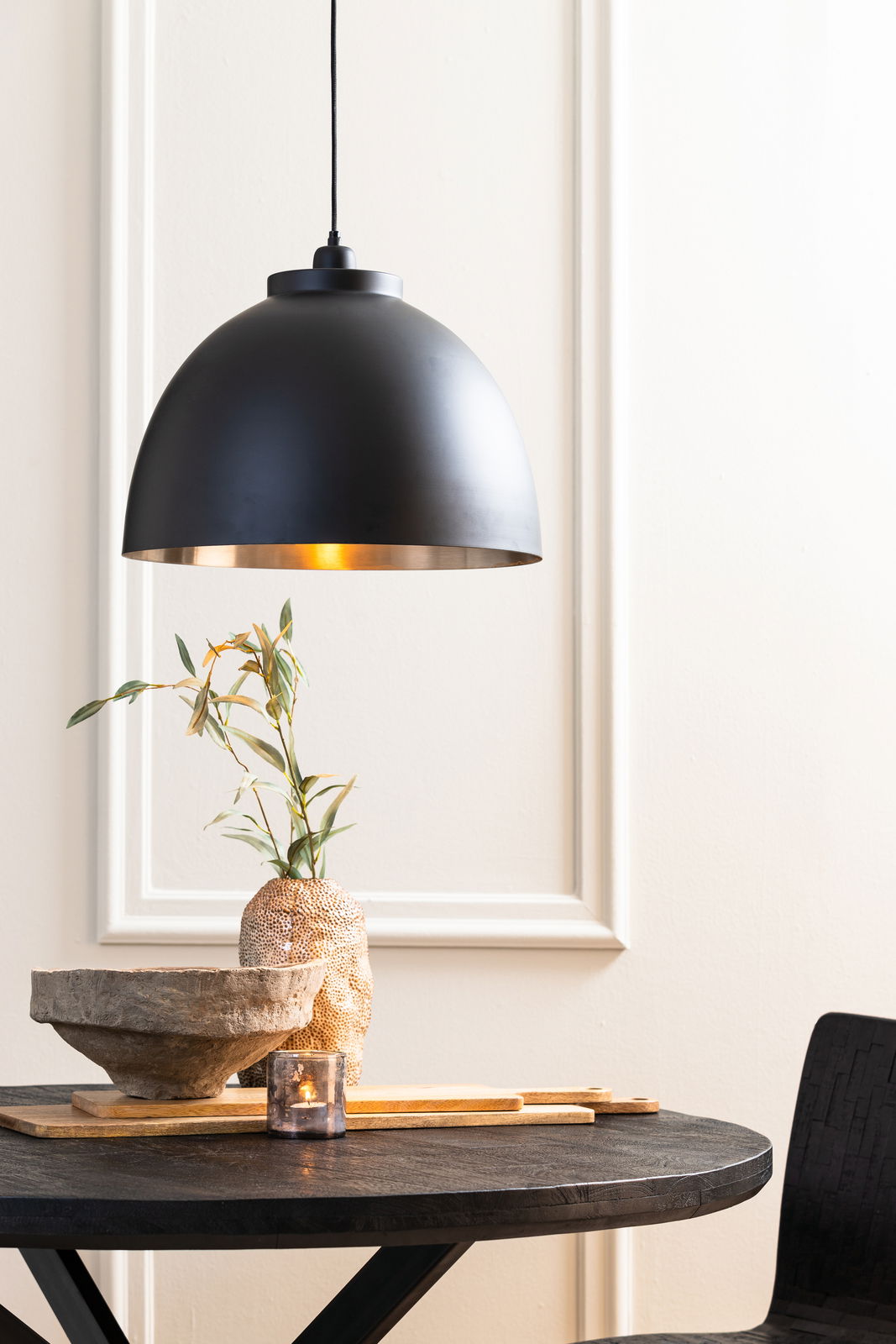 Schwarze Hängeleuchte mit goldener Innenseite über einem Tisch, seitliche Perspektive