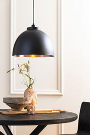 Schwarze Hängeleuchte mit goldener Innenseite über einem Tisch, seitliche Perspektive