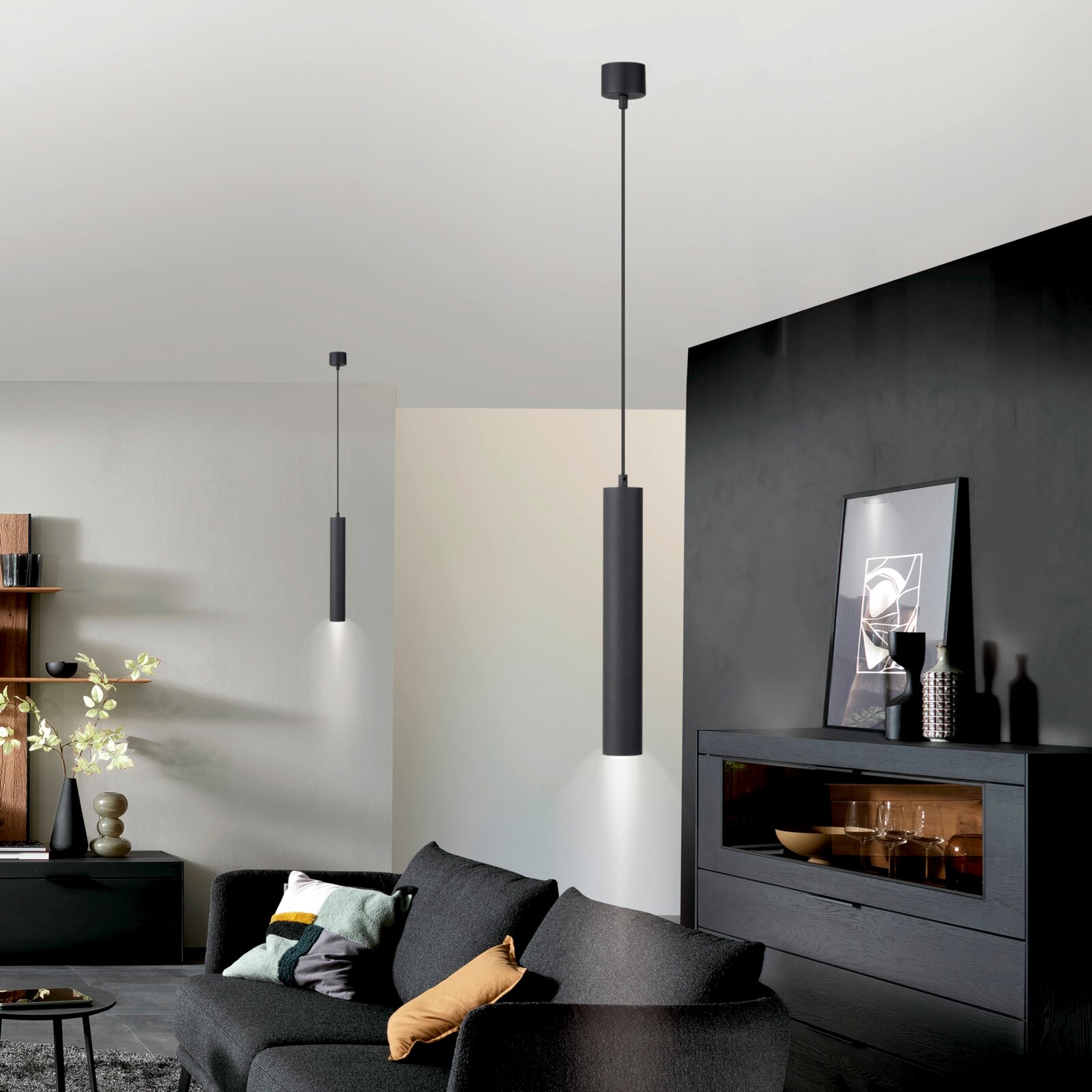 Moderne schwarze zylindrische Pendelleuchte mit direktem Lichtkegel nach unten, in einem Wohnzimmer montiert, Ansicht aus leicht niedriger Perspektive nach oben