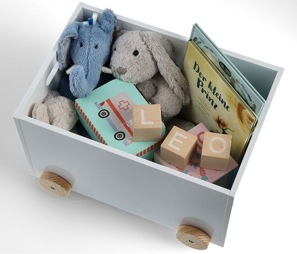 Weiße Kinder-Spielzeugkiste mit Rollen, gefüllt mit Plüschtieren, Holzklötzen und einem Buch, aus der Vogelperspektive.
