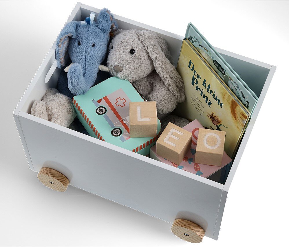 Weiße Kinder-Spielzeugkiste mit Rollen, gefüllt mit Plüschtieren, Holzklötzen und einem Buch, aus der Vogelperspektive.